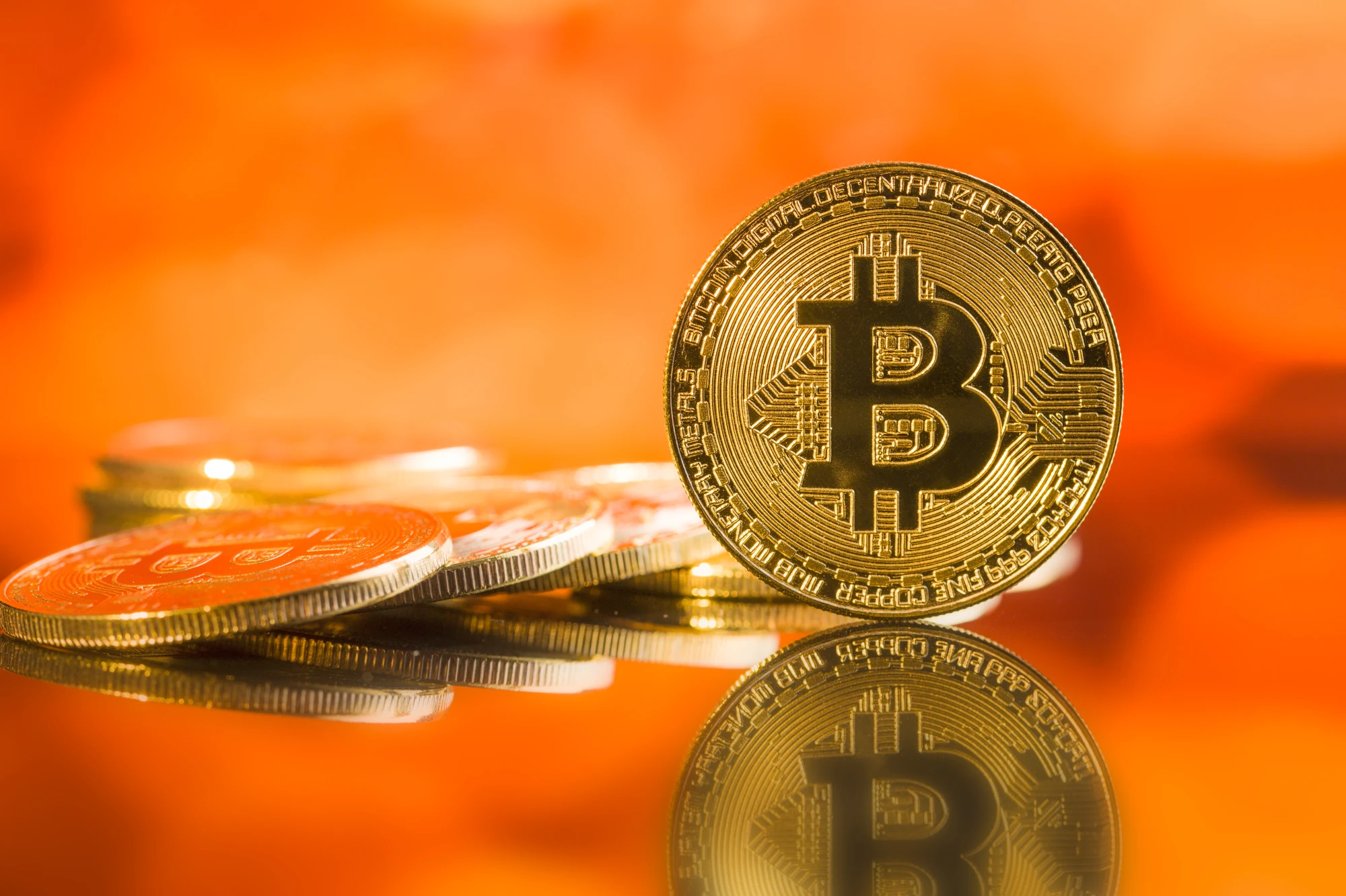 A close-up of golden Bitcoin coins reflecting on a surface with an orange